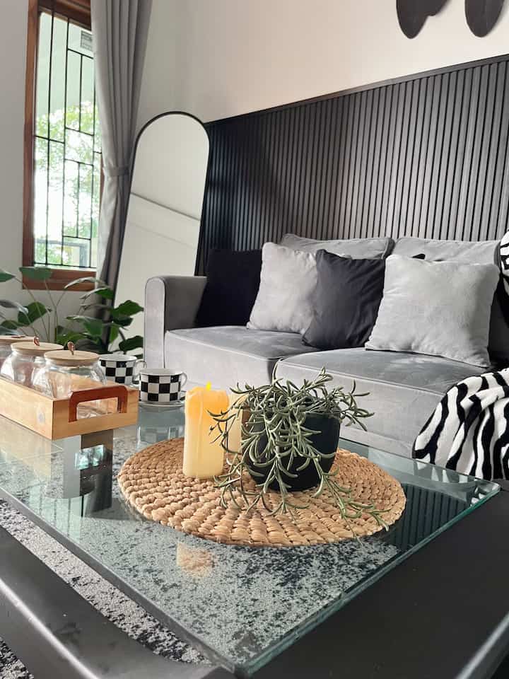Gray and black toned living room featuring a sofa, glass coffee table, plants, and candles with a natural modern atmosphere