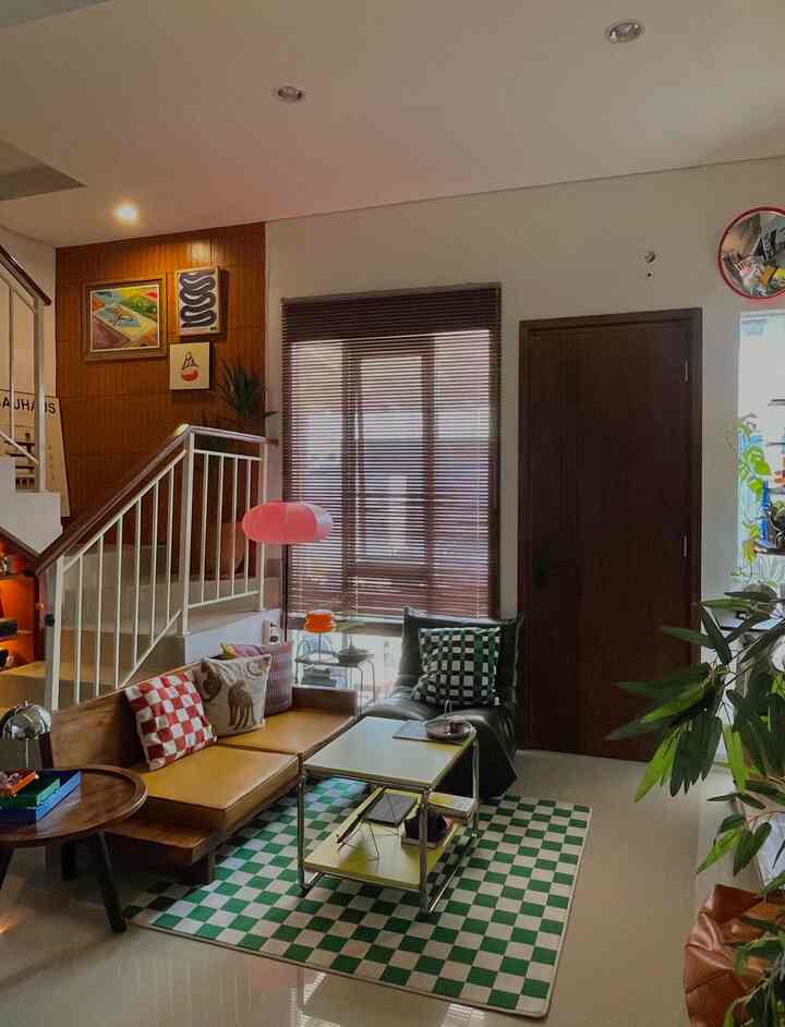 Warm-toned living room with wooden furniture, checkered rug, plants, and framed art creating a cozy atmosphere