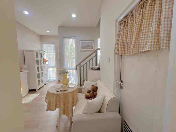 Beige and ivory toned living room featuring sofa, round table with vase, and teddy bear creating a cozy atmosphere
