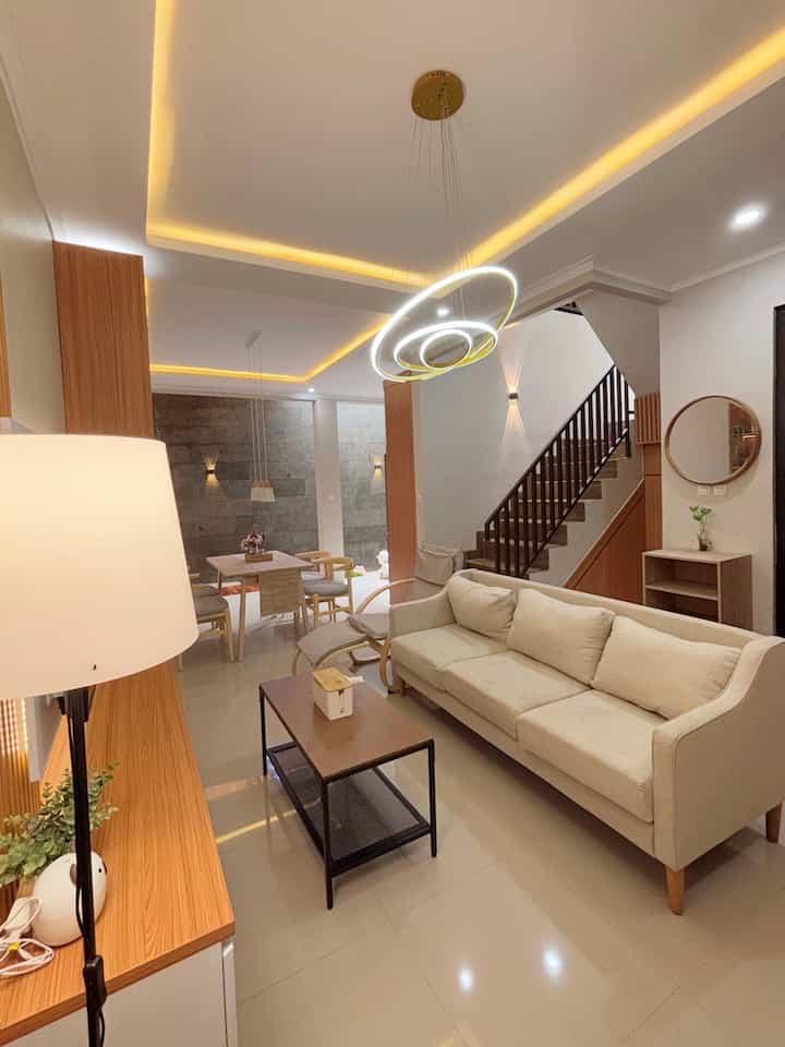 White and wood tone living and dining room featuring a beige sofa and pendant light in a simple modern style with a cozy atmosphere