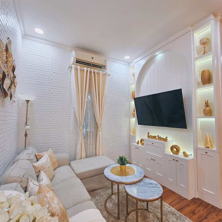 Living room with white walls and gold accents featuring beige sofa and curtains creating a warm atmosphere