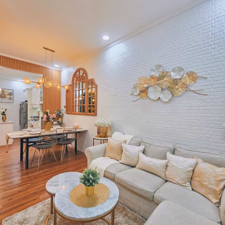 Natural modern living and dining room with white brick walls, gold accents, and wood-tone flooring creating a warm atmosphere