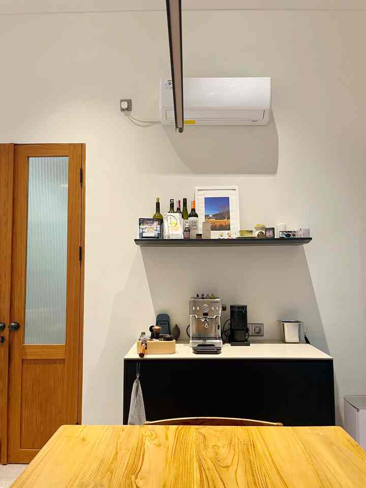 A simple home cafe in the dining room featuring a black cabinet with coffee machine, shelf, and picture frames against white walls and wood-tone dining table