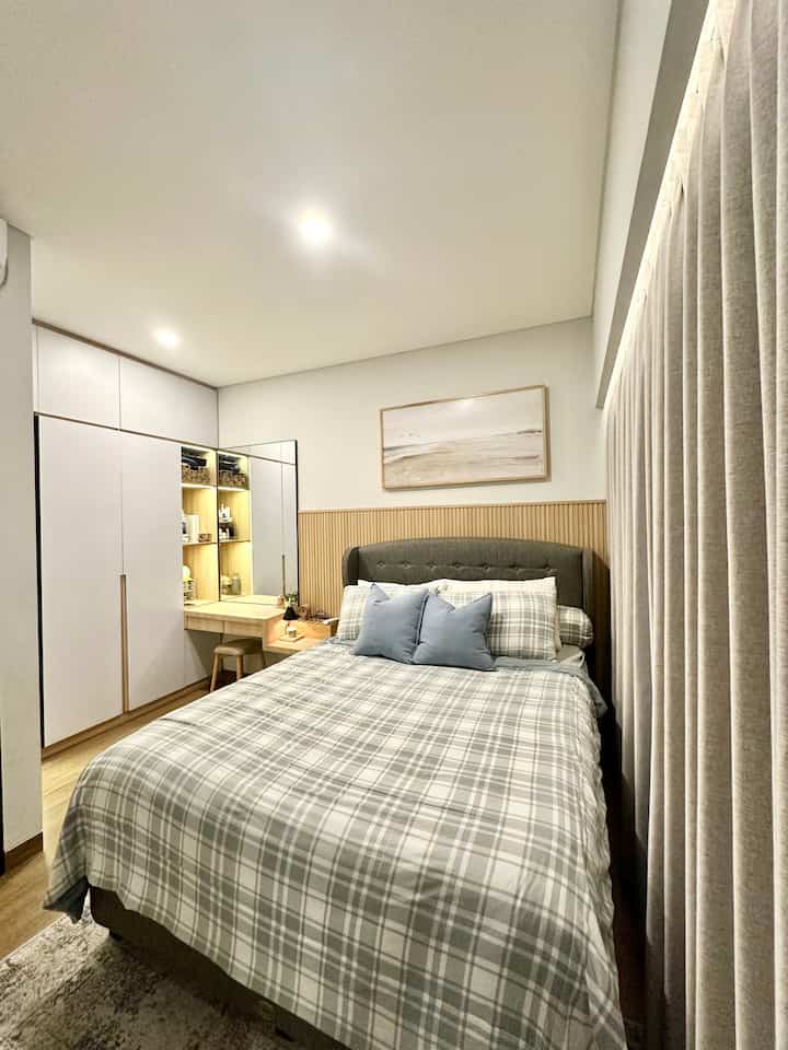 White and beige toned bedroom featuring plaid bedding and wood-tone storage, creating a simple modern atmosphere