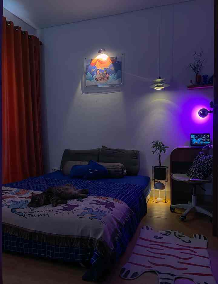 A bedroom with a blue bed and brown flooring, featuring a cat lying on the bed in a cozy atmosphere