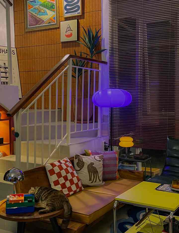 A cozy living room with wood tones and yellow accents, featuring a sofa and a cat resting on a side table