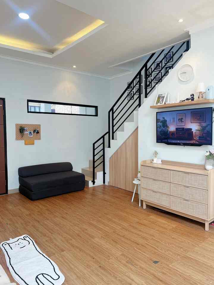 Bright living room with white walls and wood-tone flooring featuring a black sofa and TV cabinet, creating a clean atmosphere