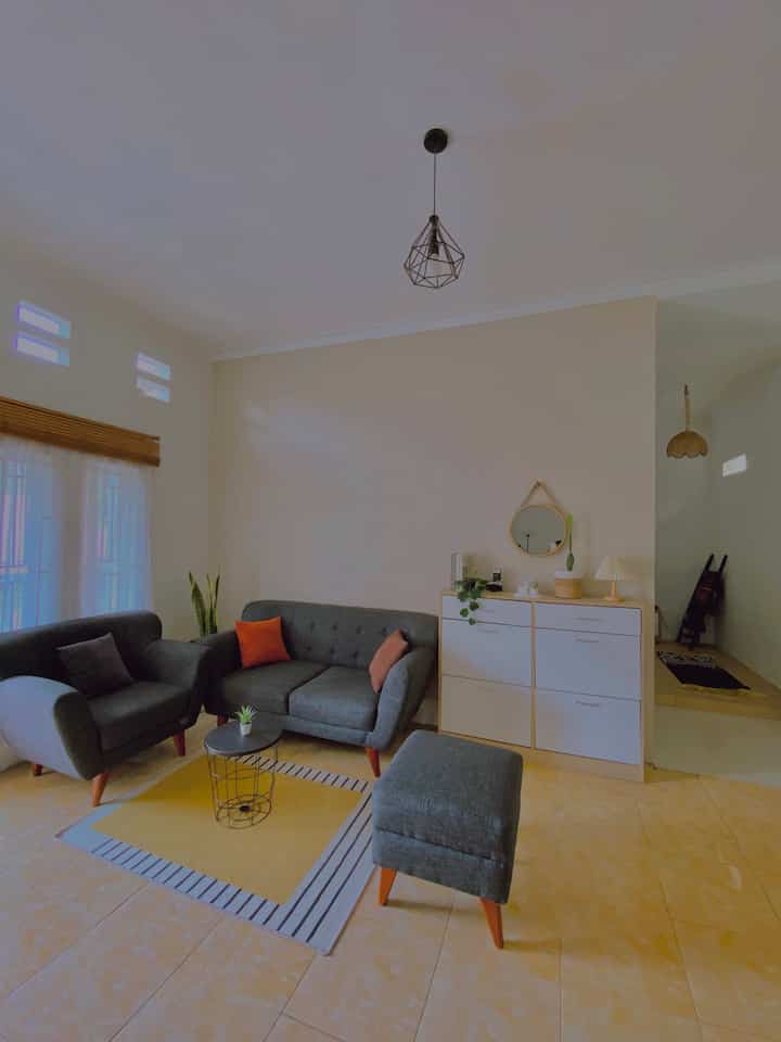 A clean two-person living room with light cream walls, gray sofa set, and black pendant light