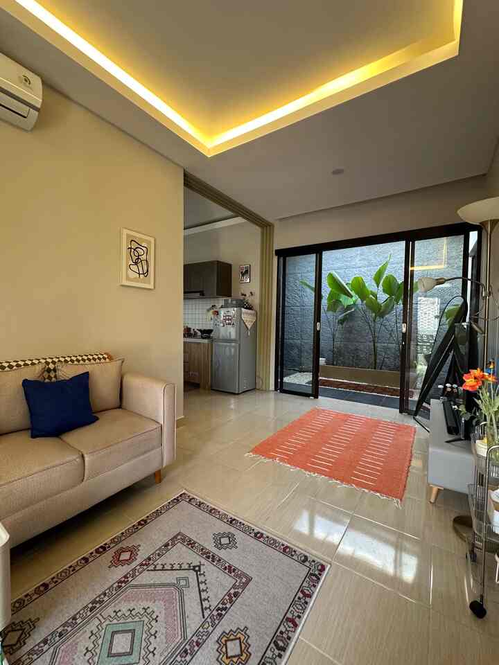 A beige-toned living room with sofa and carpets, natural light and green plants creating a cozy atmosphere