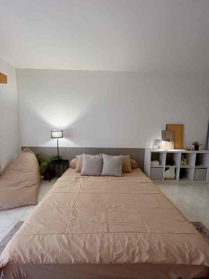 Beige-toned bedroom featuring a large bed, bean bag, and bookshelf in a simple and cozy setting