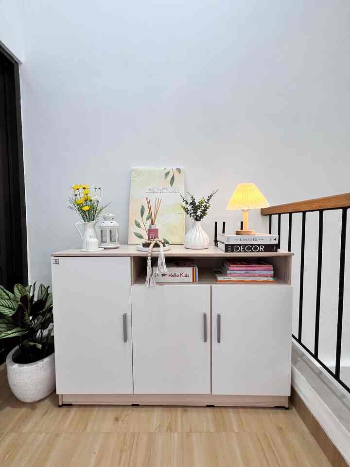 A white and natural color living room featuring a storage cabinet, table lamp, and plants arranged neatly