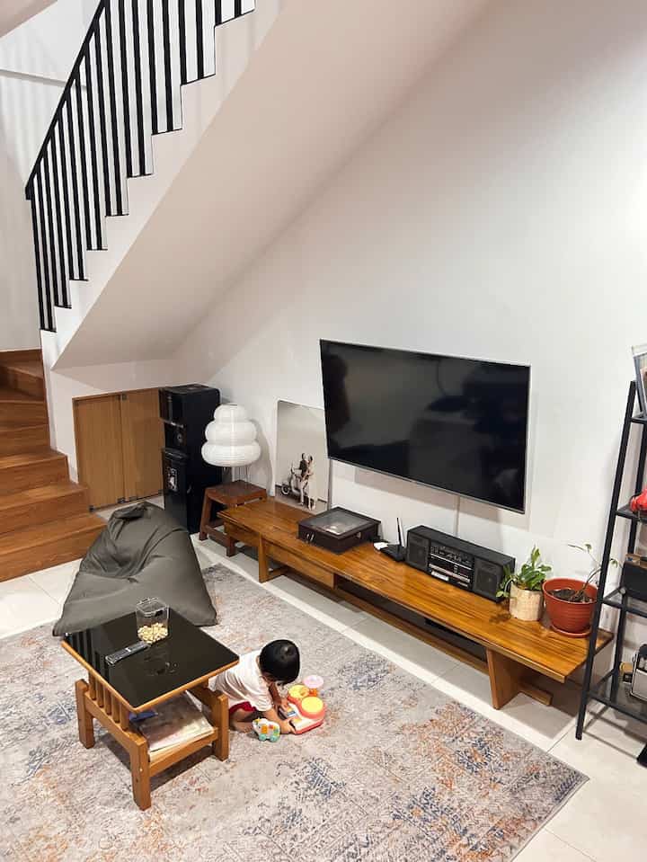 Compact living room with wood tones and white walls featuring a bean bag, TV stand, and a child playing with toys in a cozy setting