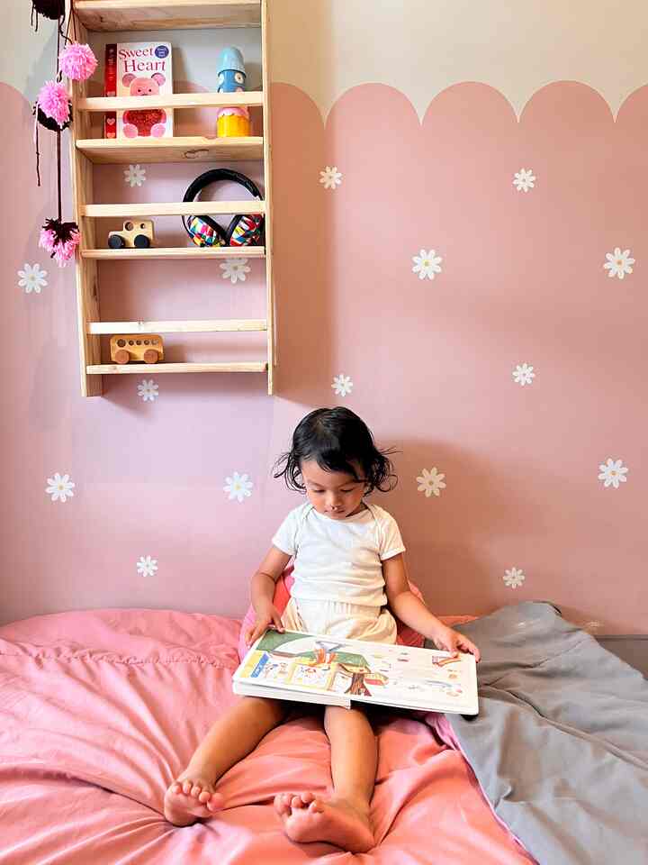 Pink-walled kids' room featuring large floor cushion with child sitting centrally reading a book, creating a cozy atmosphere