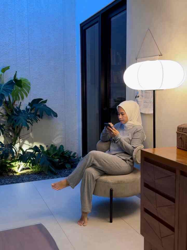 Natural and white toned living room relaxation area featuring a cozy armchair, floor lamp, and lush plants creating a tranquil atmosphere