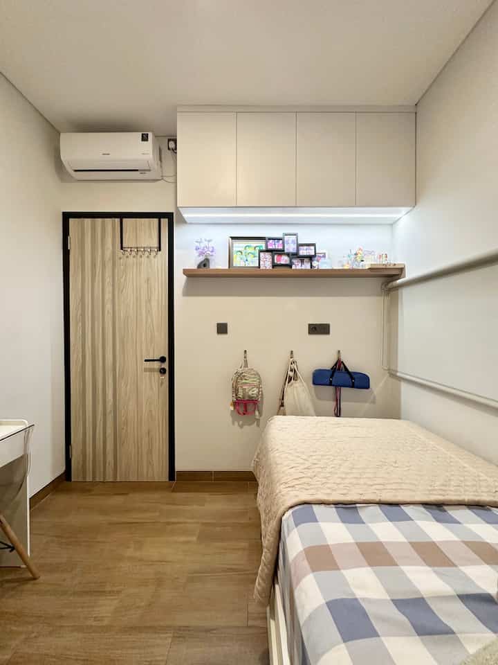 White walls and brown wood-tone floor in a compact bedroom space featuring a single bed and wall-mounted storage cabinets