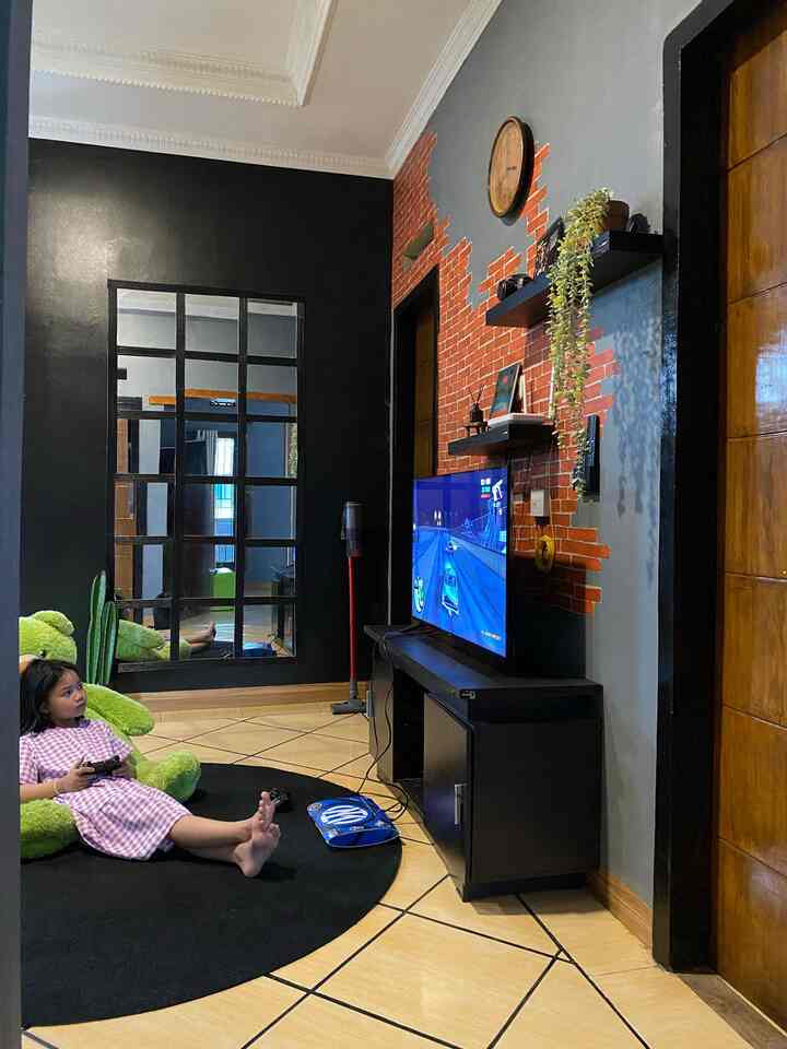 Black and brick accent living room featuring a black round carpet with a child comfortably playing video games