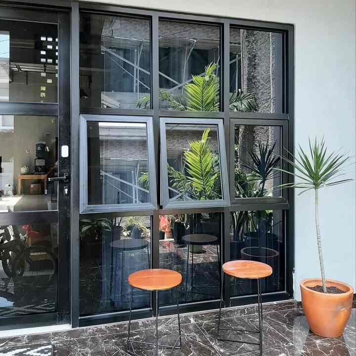Modern balcony with black window frames and brown stools, featuring natural plants with a clean atmosphere