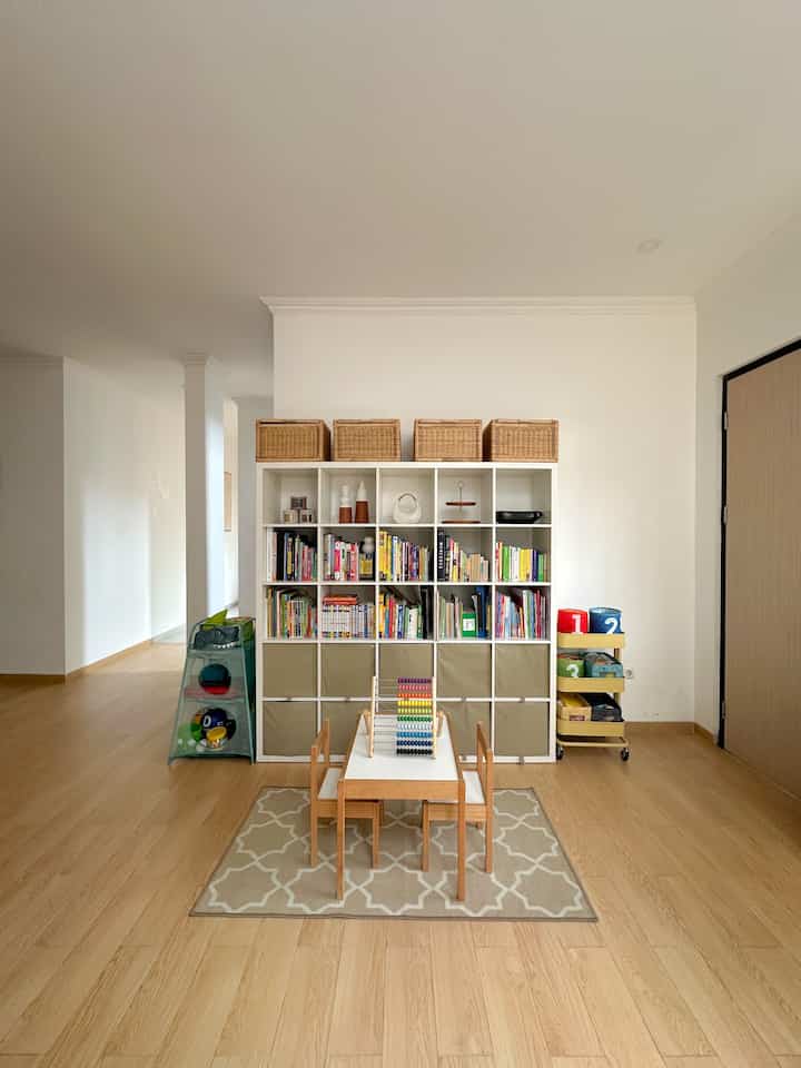 Natural kids' area with white walls, wood-tone flooring, featuring a central children's bookshelf and kids' table for reading and play