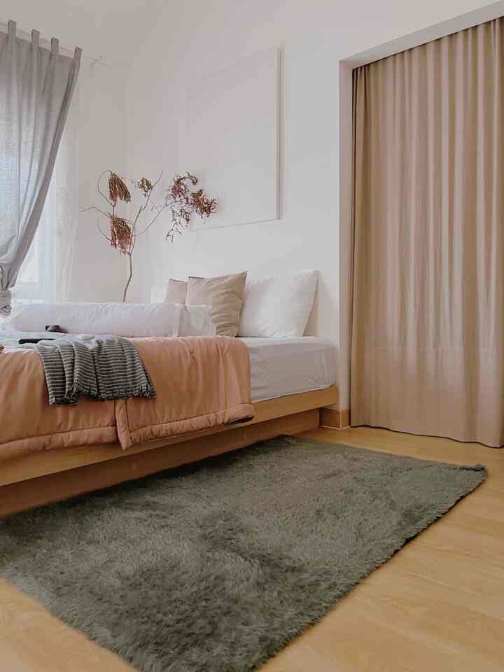 Wood tone floor and beige curtains in a white-walled bedroom with bedding, styled in Japandi aesthetic