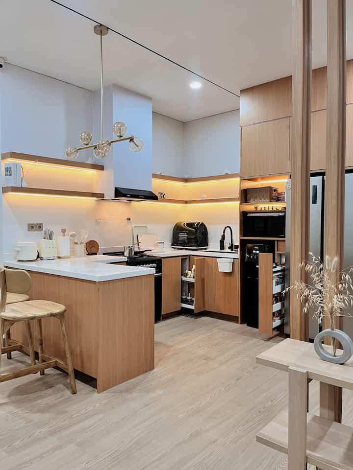 A clean and modern kitchen space with natural wood tones and white surfaces featuring pendant lighting and a kitchen island