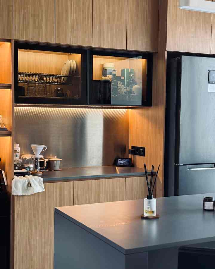 Modern kitchen with wood tones, spacious countertops and cabinets, featuring stainless steel backsplash and indirect lighting