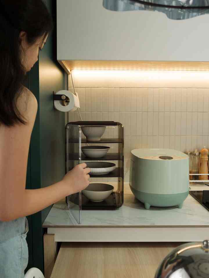 Natural color kitchen space featuring transparent storage for bowls and a mint-colored rice cooker with clean interior style