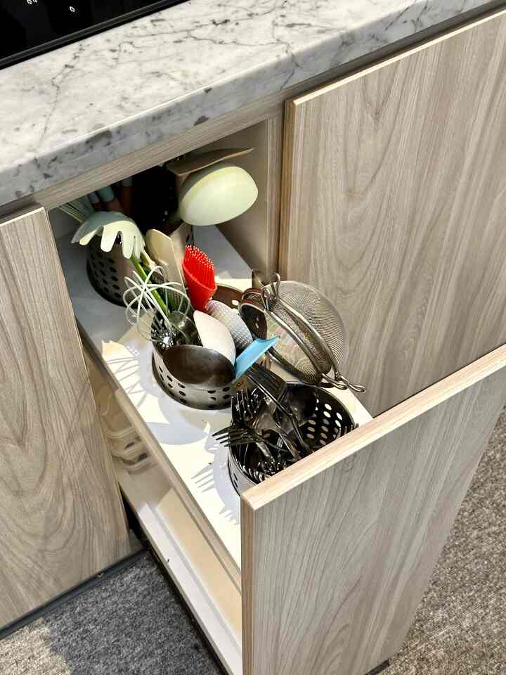 Natural colored kitchen showing cabinet drawer opened with various kitchen utensils inside