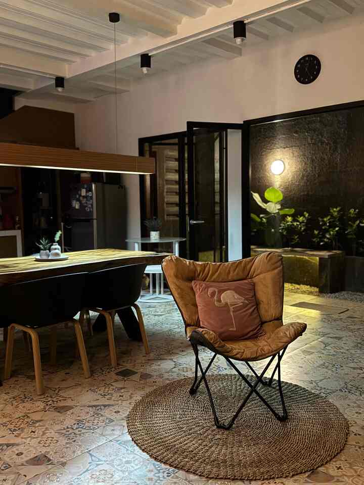 Cozy living room with warm wood tones and cafe style lighting, featuring a brown leather armchair, dining table, and chairs