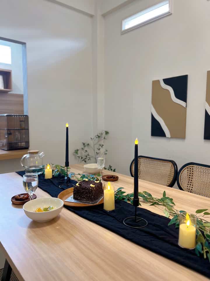 Bright white walls and wood-toned dining room with a simple black table runner and electric candles centered on the table