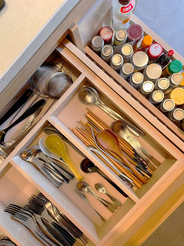 Beige and white toned kitchen drawer featuring organized cutlery and spice jars in a neat setting