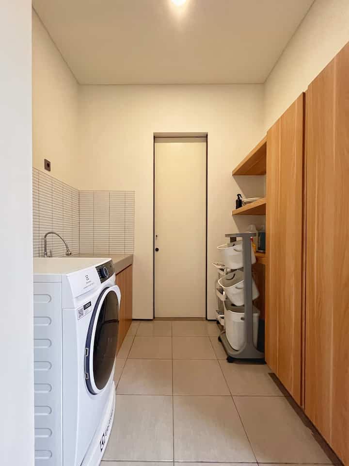 White and natural color laundry room featuring a washing machine and wooden cabinets in a clean compact space
