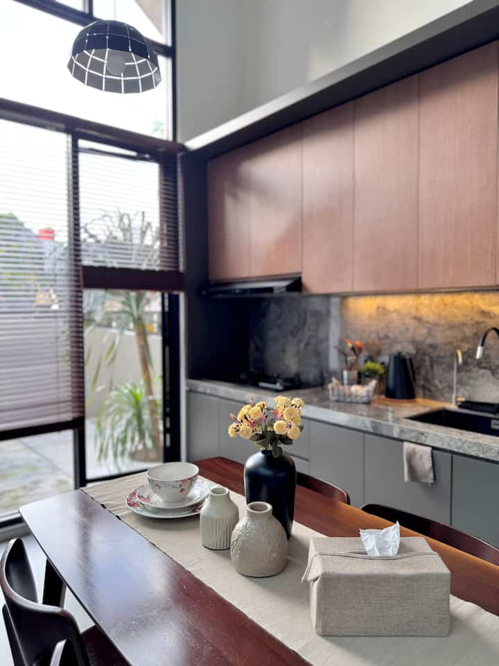 Natural wood-tone kitchen and dining room featuring a simple, minimalist dining table with decorative vases in a clean setting