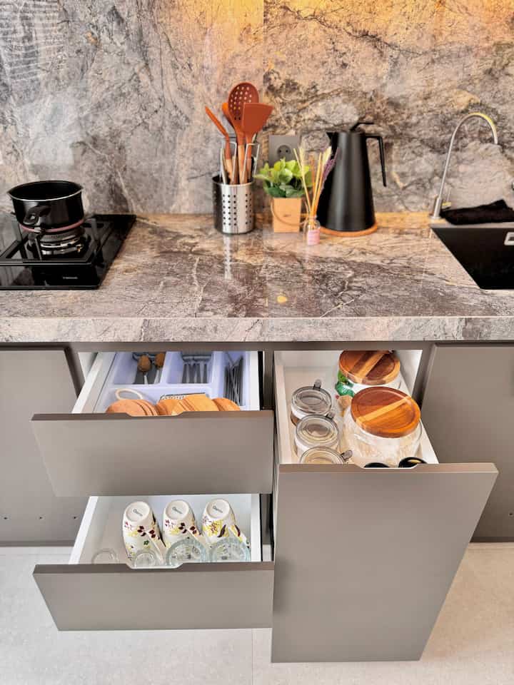 Modern kitchen with gray marble countertop and black sink, featuring wood tone accessories and organized kitchen storage drawers