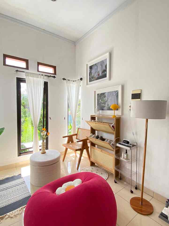 Bright white-tone room with curtains, red bean bag, and wood-tone furniture arranged in a simple living space
