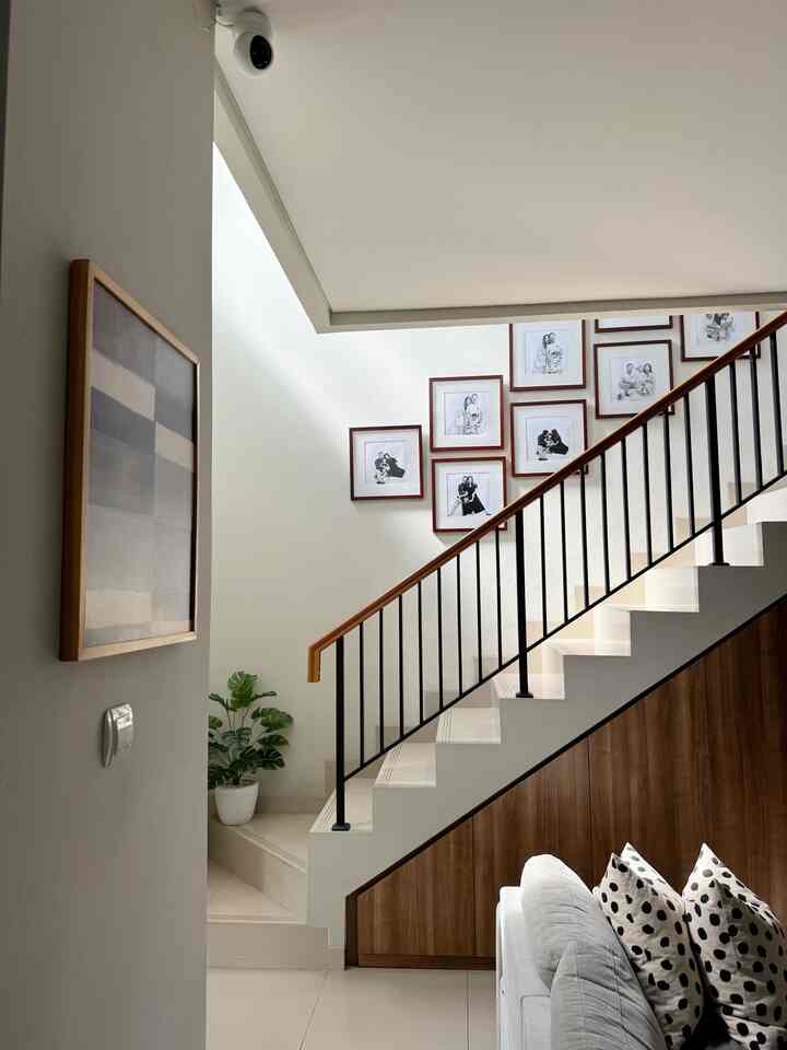 Bright white-toned staircase space featuring family photo frames on the wall, with sofa and plant in a modern living area