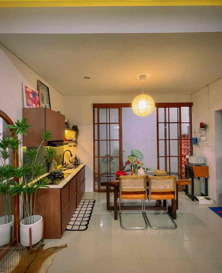 Kitchen Make Over-Midcentury Modern Style🪩
Awal menempati rumah, ruangan dapur adalah projek renovasi  kecil pertama yg dilakukan.
.
1. Merubah dapur beton bawaan developer menjadi kitchen set Hpl dgn panjang 2 meter. Budget total 11juta (diluar kompor, sink, tiles backsplash & cooker hood)
2. Memasang pintu sliding door aluminium motif serat kayu. Agar selaras dgn warna kitchen set. Budget 6jutaan untuk 2,7 x 2,3meter)
3. Mendekorasi dapur bergaya midcentury modern;
- Pemilihan Warna Hpl kayu agak gelap namun tetap warm & berkarakter. (Inspirasi dr pinterest)
-Back splash tiles hijau bercorak, sebagai sentuhan warna yg segar agar tidak monoton.
-Rak Ambalan. Bisa untuk display alat2 dapur & dekorasi ala-ala cafe agar lebih instagramable.
-Lampu gantung lampion ikea, inspirasi dr pinterest yg low budget tp berpengaruh sekali dgn ambience ruangan.
-Pop up color pada dekorasi art wall, backsplash, Vas + tanaman plastik menjuntai.
-Pohon Artifisial Dracaena setinggi 180cm sbg pemisah ruang dgn living room agar dapur terlihat semakin estetik.
.
#MyDreamKitchen #KitchenRenovation #KitchenStyling #KitchenTransformation #RenovasiDapurStandarDeveloper #KursiMakanStainless #FurniturMidcenturyModern #LampuLedDapur #LampuGantungDapur #PohonArtifisial 