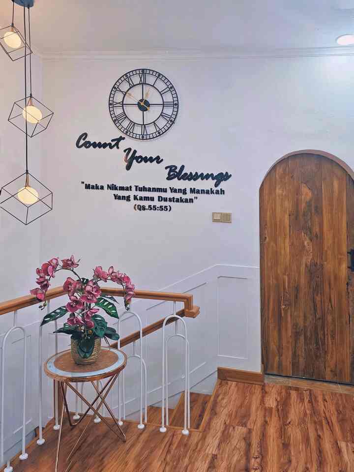 Bright white-walled entrance space featuring wood tone flooring and door, with a large clock and inspirational text wall decor