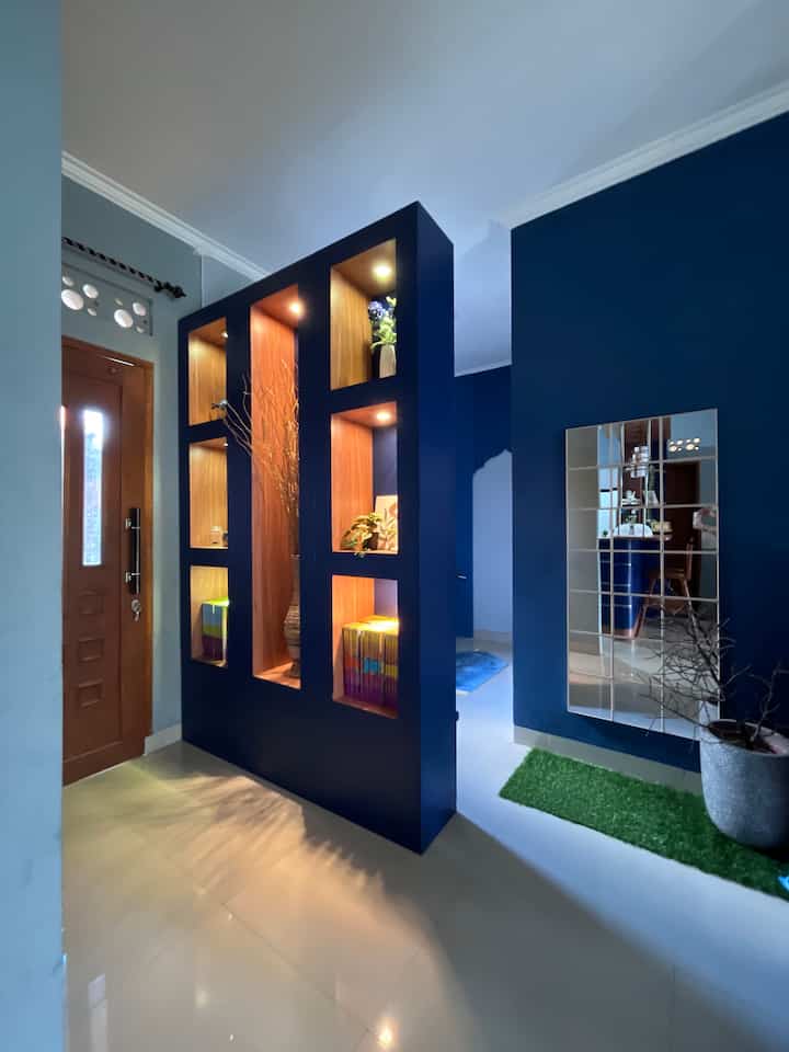 Area ini merupakan area masuk/ koridor rumah navy ini, kami buat partisi dari material papan multi yang dilapisi HPL dengan dekorasi cantik di setiap rak nya. 
Partisi ini menjadi multifungsi karena selain untuk menyimpan dekorasi estetik bisa juga dijadikan rak buku dan bagian belakangnya untuk perlengkapan alat shalat sebagai penyekat antara pintu utama dengan mushola mini. 
Beberapa perintilan seperti tanaman dan akar manon menjadi bagian dekorasi utama partisi ini ditambah dengan pemasangan lampu downlight di setiap trap raknya. 
Sebelah partisi kami juga menempel cermin kotak dan pot teraso serta tanaman dahan kering yang menambah ruangan semakin estetik. 
#DekorasiEstetik
#SmallDecorItems
#DecorativeItems
#Koridor
#Partisi
#musholamini
#Cerminestetik
#cerminkotak
#akarmanon
#areamasukrumah