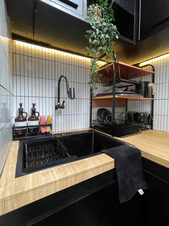 Modern kitchen sink area in black and wood tones, featuring tiled backsplash and storage shelves in a cozy corner setup