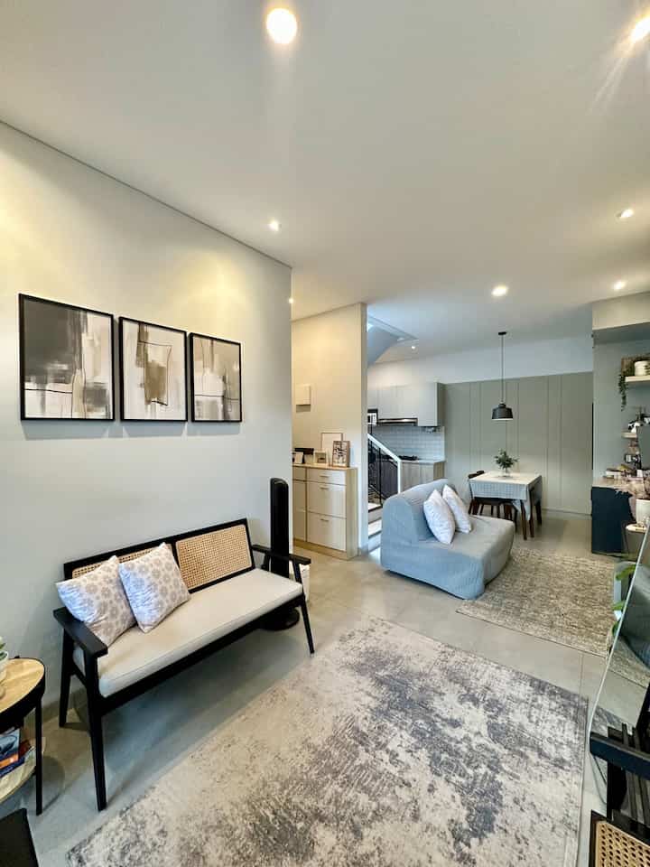 Bright white and beige toned living room featuring modern sofas, carpets, and abstract wall decor with a clean, spacious atmosphere