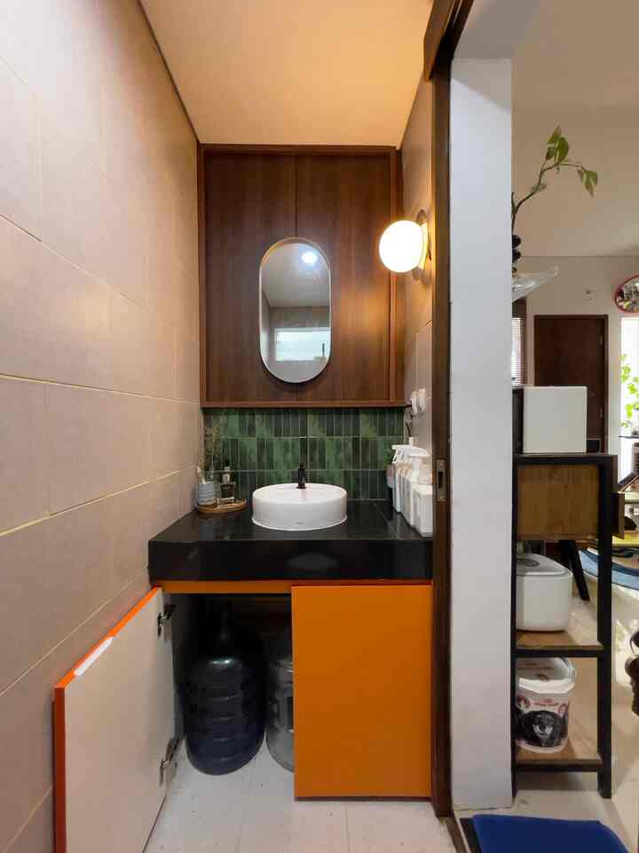 Green tiled backsplash and wood-tone wall panel feature above orange lower cabinet and white washbasin in compact washroom