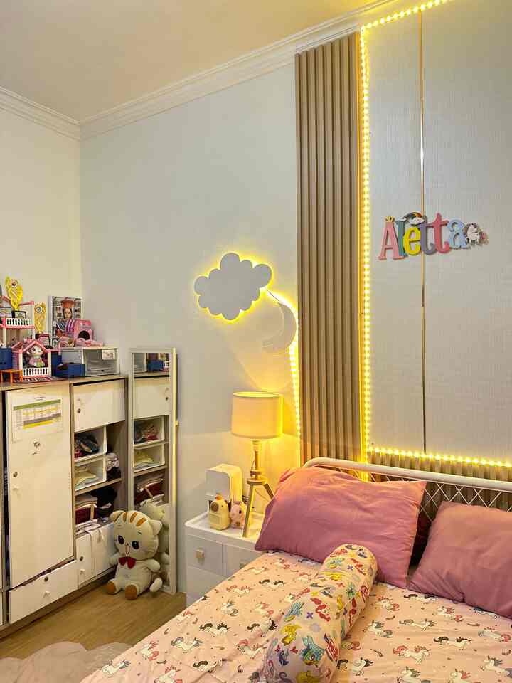 Pink and white toned kids' bedroom featuring bed, storage cabinet, and warm lighting creating cozy atmosphere