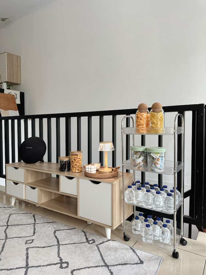 A living room with white and wood tones featuring a TV stand and a plastic storage shelf, arranged neatly in a cozy atmosphere