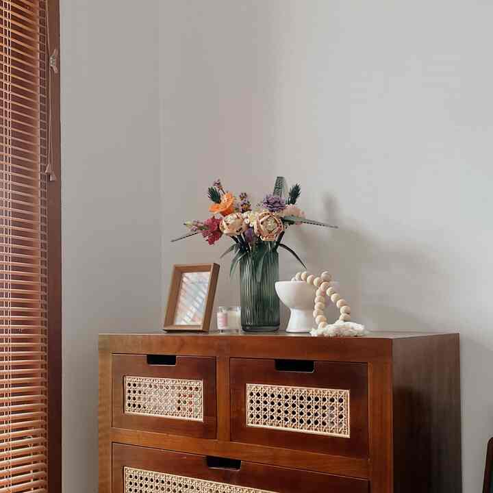 Natural and simple living room corner featuring white walls and a brown vintage dresser with decorative items