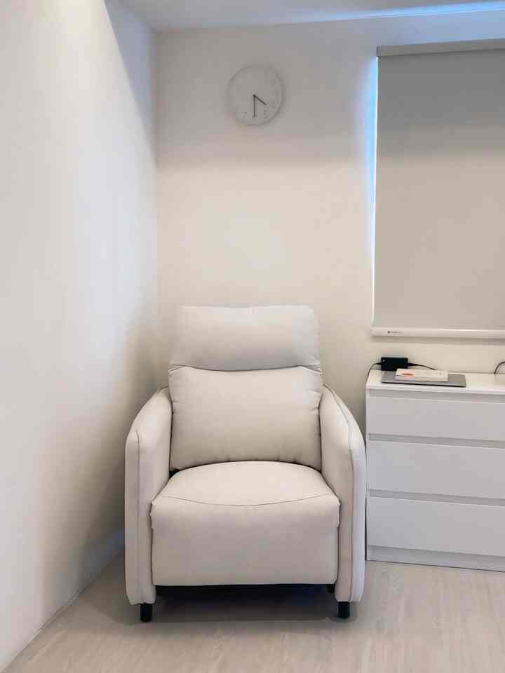 White-toned bedroom featuring a central white recliner sofa and white dresser on the right in a minimal style