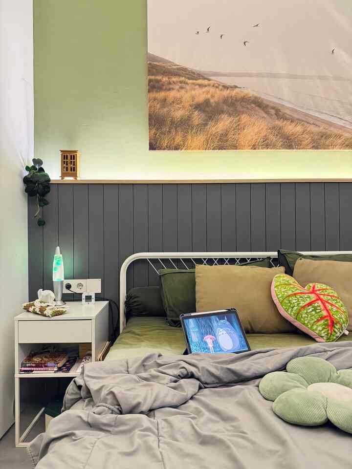 Green and gray toned bedroom featuring white metal frame bed with assorted cushions in a cozy setting