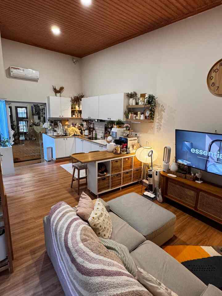 Natural wood tone and white kitchen blend in an open living room featuring a gray sofa and TV stand with a warm night vibe