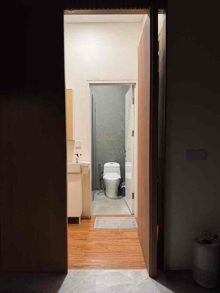 A simple bathroom at the end of a narrow hallway with white walls and wood tone flooring