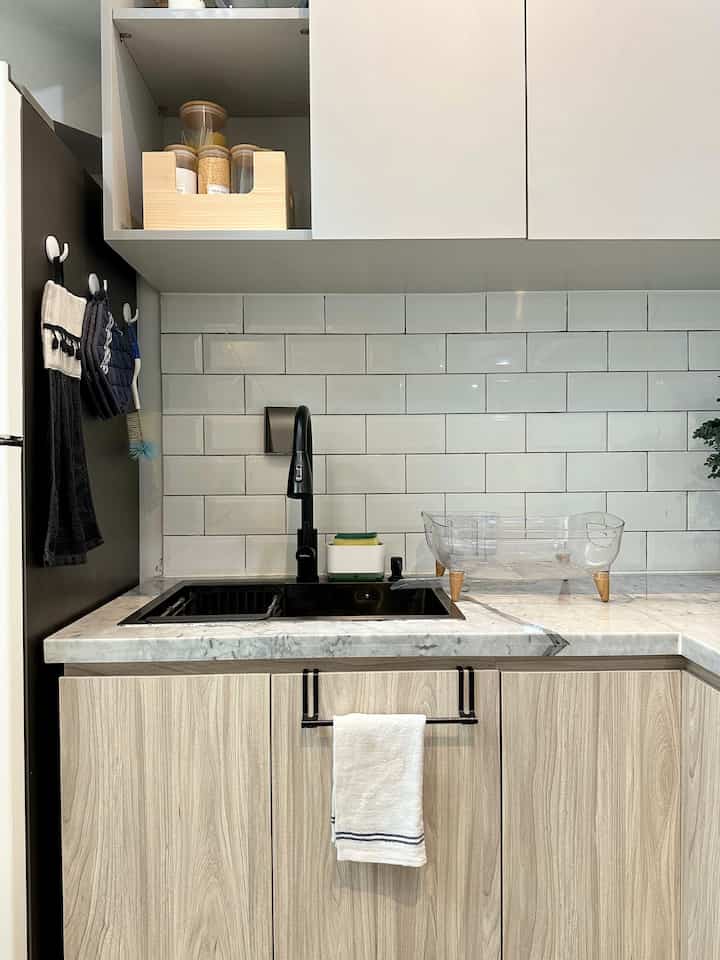 Modern kitchen space with white tile backsplash, wood-tone lower cabinets, and black sink with faucet
