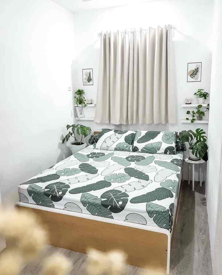 Bright white and brown toned bedroom featuring leaf-patterned bedding and multiple plants creating a clean, natural atmosphere